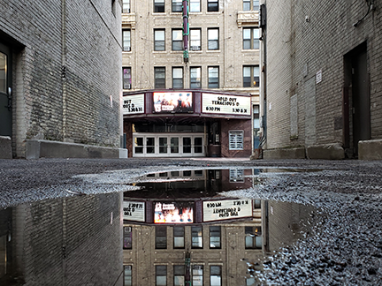 low angle photo looking at the outside of a movie theatre and it's reflection in a puddle