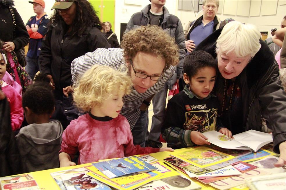 Kids and adults look through books on a table.