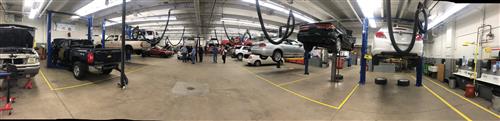 View of auto shop with cars and trucks in lifts on the right and left sides.